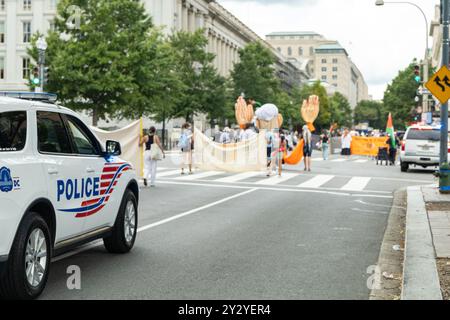 Washington DC, USA - 19.08.2024: Ein Polizeiauto parkt am Straßenrand. Eine Gruppe von Leuten marschiert auf der Straße Stockfoto