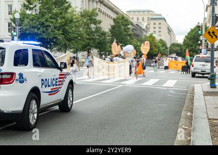 Washington DC, USA - 19.08.2024: Ein Polizeiauto parkt am Straßenrand. Eine Gruppe von Leuten marschiert auf der Straße Stockfoto