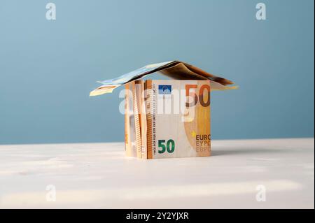 Konzeptionelles Bild von Immobilien, Hypotheken, Mieten und Wohngebäuden. Haus aus Euro-Banknoten auf blauem Hintergrund mit Kopierraum. Stockfoto