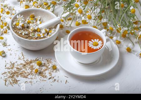 Ländliche Stillleben - Tasse gebrühten Kamillentee auf dem Hintergrund eines Straußes von Gänseblümchen, Nahaufnahme Stockfoto