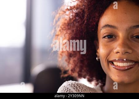 Lächelnde Frau mit lockigem Haar im Büro, mit weißem Pullover, Nahaufnahme Porträt, Kopierraum Stockfoto