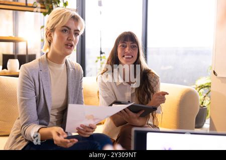 Im Büro, in der Hand von Dokumenten und Tablet, diskutieren zwei Frauen über kreative Geschäftsideen Stockfoto