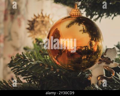Goldenes gelbes Weihnachtskugel-Ornament dekoratives Element wird an Weihnachtsbaum mit Bokeh-Licht gehängt, Stockfoto