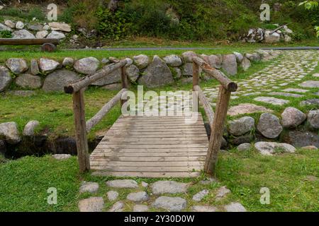 Rustikale Holzbrücke über einen kleinen Bach mit Steinweg Stockfoto