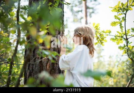 Ein Teenager umarmt einen Baum im Wald. Umarmen und berühren Sie Bäume, um Stress zu reduzieren und sich mit der Natur zu verbinden. Stockfoto