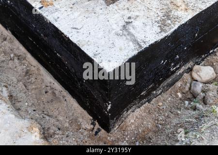 Die Ecke eines Streifenfundaments aus Stahlbeton ist mit einer schützenden schwarzen Bitumenkomposition bedeckt, das Landhaus befindet sich im Bau Stockfoto