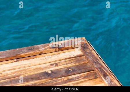 Die Ecke eines leeren Holzpiers befindet sich auf dem unscharfen blauen Meerwassergrund Stockfoto