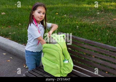 Junges Mädchen mit grünem Rucksack auf Parkbank in lässigem Outfit Stockfoto