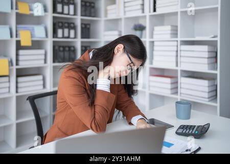 Geschäftsfrau plant eine Finanzprüfung, prüft Dokumente, während sie gegen das Burnout-Syndrom kämpft Stockfoto