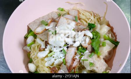 Asiatische gelbe Nudeln, Schweinefleisch und Krabbenfleisch, Knödel und Gemüse in rosa Schüssel. Stockfoto
