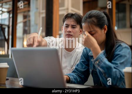 Ein gestresster und unzufriedener asiatischer Mann diskutiert Probleme mit seiner Kollegin und drückt Frustration über Fehler während eines Treffens in einem Café aus Stockfoto