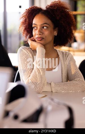 Im Büro sitzt eine lächelnde Frau in einem gemütlichen Pullover am Schreibtisch in kreativem Schreibgeschäft Stockfoto