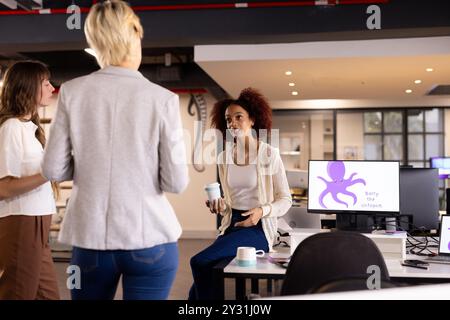 Zusammenarbeit in modernen Büros, multirassische Frauen diskutieren Projektideen mit Computer und Kaffee Stockfoto