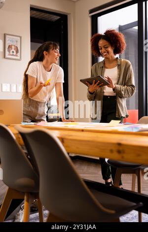 Über Ideen diskutieren, zwei Frauen aus verschiedenen Rassen, die im Büro mithilfe von Tablets und Haftnotizen zusammenarbeiten Stockfoto