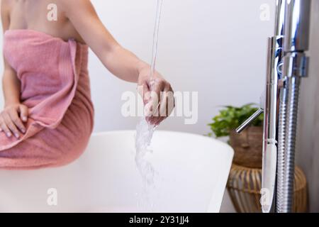 Zu Hause, entspannend in der Badewanne, Frau im Handtuch berührt fließendes Wasser im Spa-Setting Stockfoto