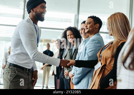 Kreative Geschäftsleute begrüßen sich gegenseitig mit einem Handschlag in einer modernen Konferenzumgebung. Vielfältige Gruppe von Menschen, die interagieren und lächeln. Stockfoto