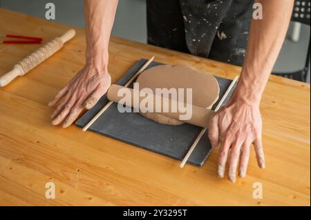 Nahaufnahme von Töpferhänden, die Ton ausrollen. Stockfoto