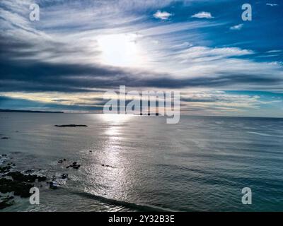 Eine wunderschöne Meereslandschaft mit Sonnenuntergang über dem Horizont, Reflexionen auf das ruhige Meer und einen dramatischen wolkengefüllten Himmel. Stockfoto