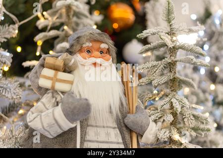 Eine Weihnachtsinstallation mit dem Weihnachtsmann am Fuße eines festlich geschmückten Weihnachtsbaums im großen Einkaufszentrum. Selektiver Fokus. Stockfoto