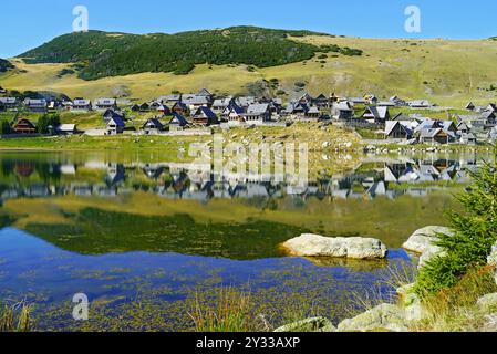 Landschaft vom Ufer des Prokoško-Sees, Bosnien und Herzegowina: Ein Feriendorf mit Hütten im traditionellen Stil und seine Reflexion im Wasser Stockfoto