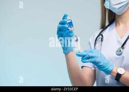Ein medizinisches Fachpersonal in Peelings und Handschuhen bereitet eine Spritze mit einer blauen Flüssigkeit vor. Sie tragen eine Maske und haben ein Stethoskop um den Hals Stockfoto