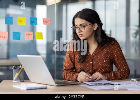 Ernsthaftes Denken und konzentrierte Geschäftsfrau hinter Papierarbeit im Büro. Ein Mitarbeiter des Unternehmens vergleicht die Daten des Berichts mit Dokumenten, ein Buchhalter oder ein Wirtschaftsprüfer bei der Arbeit. Stockfoto