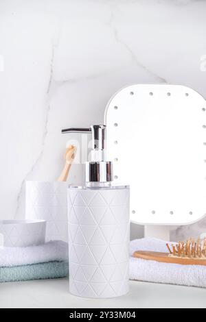 Badezimmerregal mit einfachem weißem Hintergrund. Spender für Seife, Duschgel, Seifenschale, Glas mit Zahnbürsten, Stapel Handtücher auf der Arbeitsplatte. Modell für Stockfoto