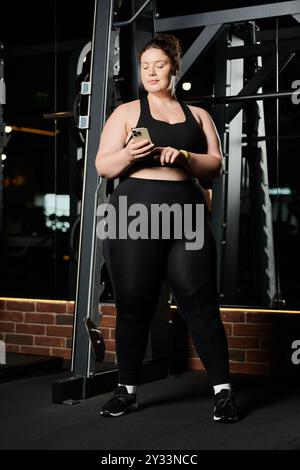 Eine selbstbewusste junge Frau nimmt ihre Stärke an und nimmt sich einen Moment Zeit, um ihr Handy während eines stärkenden Workouts zu überprüfen. Stockfoto