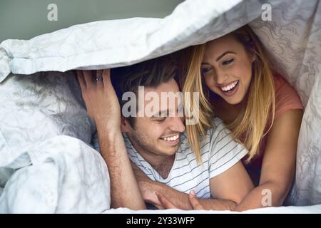 Liebe, lache und Decke mit einem Paar im Schlafzimmer für Romantik, Bindungen oder Heirat. Flitterwochen, Kurzurlaub und Hausvermietung mit Mann und Frau im Urlaub Stockfoto