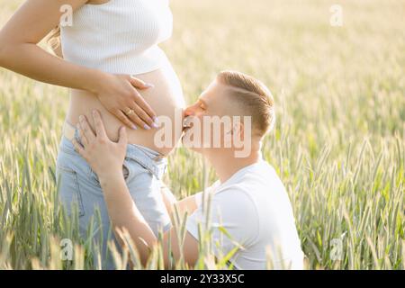 Ein glücklicher Mann küsst eine schwangere Frau auf einer Wiese Stockfoto