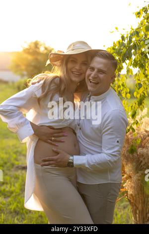 Der Mann hält die schwangere Frau in den Armen, ihr Lächeln erleuchtet den Himmel Stockfoto
