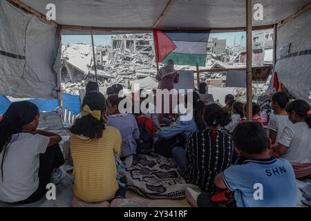 Gaza, Gaza, Palästina. September 2024. Die palästinensische Lehrerin Israa Abu Mustafa ergriff die Initiative, ein Klassenzimmer mit 30 Schülern in einem Zelt auf den Ruinen ihres zerstörten Hauses einzurichten, um Kinder zu unterrichten, wenn das neue Schuljahr beginnt und die Schüler aufgrund des Krieges nicht regelmäßig zur Schule gehen. Im Lager Khan Younis im südlichen Gazastreifen, 12. September 2024. Das palästinensische Bildungsministerium gab zu Beginn des Studienjahres 2024/2025 eine Erklärung ab, in der es heißt, dass Studenten im Gazastreifen ihr Recht auf Bildung entzogen werden. Mehr als 650.000 männlich und f Stockfoto