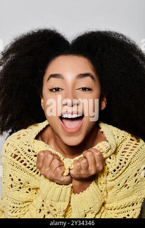 Eine junge Frau strahlt vor Glück und zeigt ihr lockiges Haar und ihren leuchtend gelben Pullover. Stockfoto