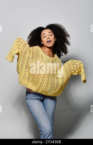 Eine junge Frau mit lockigem Haar zeigt ihren verspielten Geist, während sie einen gelben Pullover trägt. Stockfoto