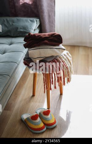 Ein Stapel warmer Kleidung auf einem Sessel neben Sofa und Hausschuhen. Gemütliches Zuhause Stockfoto