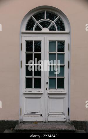 Eine hohe bogenförmige Holztür im Vintage-Design mit mehreren Glasscheiben und leicht verwitterter weißer Farbe. Stockfoto