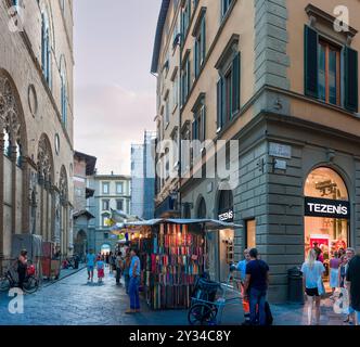 Eine lebhafte Abendszene in der Via Calzaiuoli in Florenz, Italien, wo Einheimische und Touristen durch eine enge Straße schlendern, die von Marktständen gesäumt ist Stockfoto