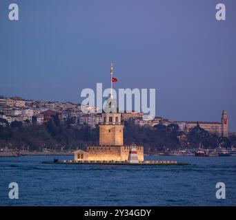 Der ikonische Maidens Tower Kiz Kulesi steht in der Abenddämmerung hoch in der Bosporus-Straße. Die türkische Flagge weht stolz auf dem Turm mit Blick auf Istanb Stockfoto