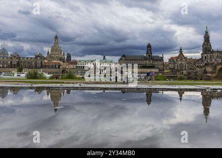 Die Dresdner Silhouette mit dunklen Wolken hinter der Kirche unserer Lieben Frau spiegelt sich in einer Pfütze auf dem Elbradweg, Elbradweg, Dresden, Sächsisch Stockfoto