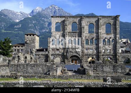 Blick auf Fassadenreste von Mauerruinen des antiken römischen Theaters mit Fensterbögen im Freilichtmuseum Aosta im Aostatal, im Hintergrund Berg Stockfoto