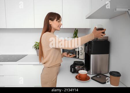 Schöne junge glückliche Frau, die in der Küche im Büro Bohnen in die Kaffeemaschine bringt Stockfoto