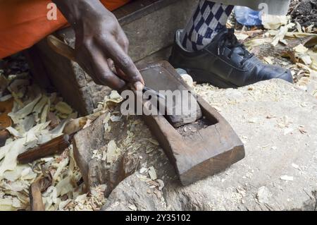 Kenianische Bildhauer schärfen einen Meißel auf einem Bimsstein in einer Genossenschaft in Mombasa Stockfoto