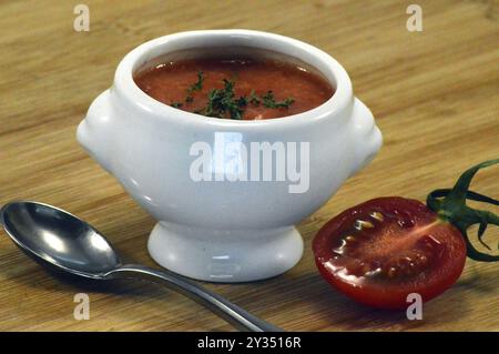 Tomatencreme in einer weißen Schüssel mit einem Löffel und einer Kirschtomate Stockfoto