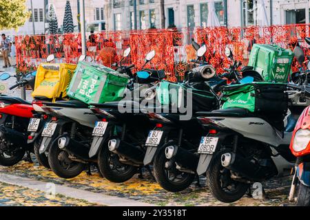In einer belebten Gegend von Lissabon stehen mehrere Lieferroller an, darunter Glovo und Uber Eats Stockfoto