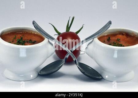 Tomatencreme in einer weißen Schüssel mit einem Löffel und einer Kirschtomate Stockfoto