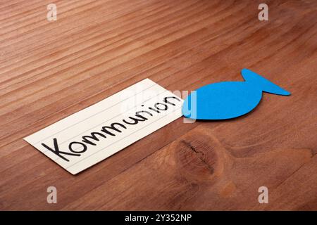 Kommunion. Deutsches Wort. Blauer Fisch in der Ecke. Verlegung auf Holz. Freier Platz für Text. Stockfoto