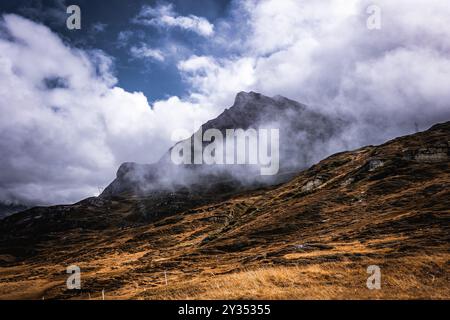 Eine Berglandschaft mit Wolken, die teilweise den Gipfel bedecken, und Trockenrasen im Vordergrund. Stockfoto