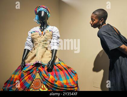 London, Großbritannien. September 2024. Museumsangestellte Kimberley mit „Queen Joyce“ von Karen Arthur, 2022, mit dem Kleid, das nach der Mutter des Künstlers benannt wurde, die sie als Frau mit afrokaribischem Erbe geformt hat und Stoffe mit vielen verschiedenen Geschichten kombiniert. Die neue Ausstellung „All our Stories: Migration and the Making of Britain“ eröffnet heute mit einer Pressevorschau im Migration Museum in Lewisham. Die neue Ausstellung zeigt, wie Migration das Wesen in Großbritannien geprägt hat - als Individuen, als Gemeinschaften und als Nation. Quelle: Imageplotter/Alamy Live News Stockfoto