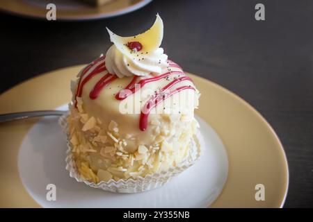 Feiner runder Mini-Biskuit-Kuchen mit Marzipans, Mandeln und Creme, dekoriert mit roter Glasur auf einem Teller und einem dunkelbraunen Tisch, festliches Dessert für den Urlaub Stockfoto