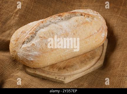 Studio-Aufnahme eines einzelnen Sauerteiglaibs auf einem Holzschneidebrett, das vor weißem Hintergrund ausgeschnitten wurde - John Gollop Stockfoto